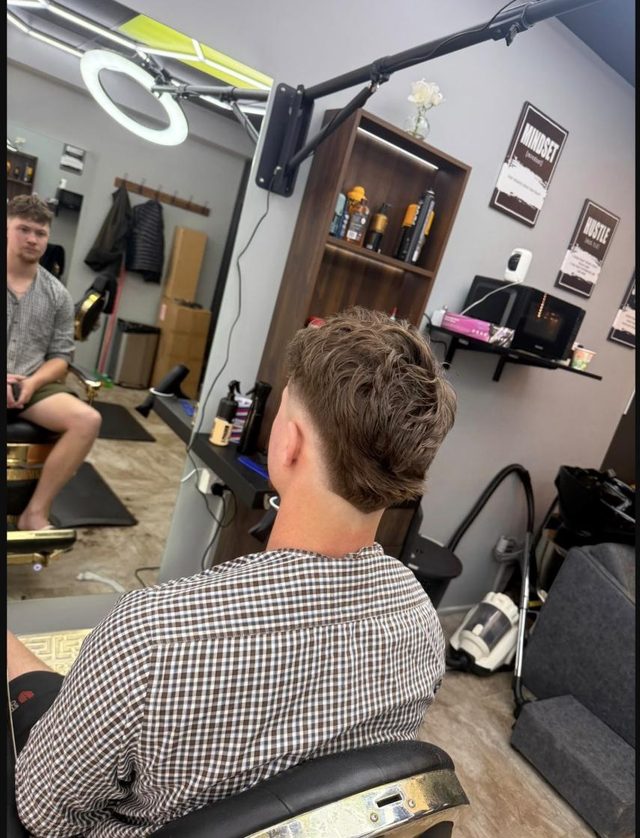 A fresh low burst fade at Fade Shack Barbers, Orewa, with the barber shop mirrors and product shelf behind.