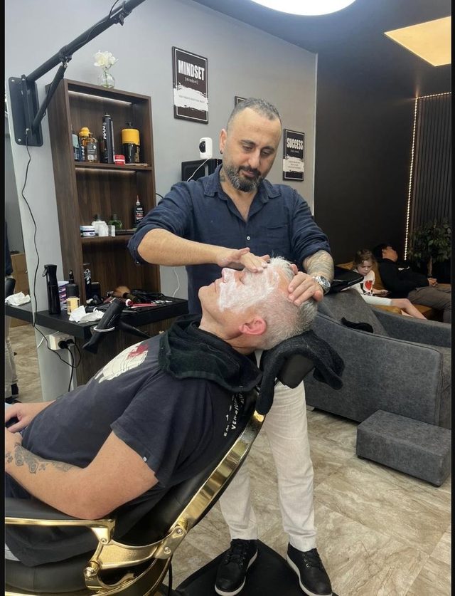 A barber working a traditional Turkish hot towel shave on a reclined client in the gold barber chair at Fade Shack Barbers, Orewa.