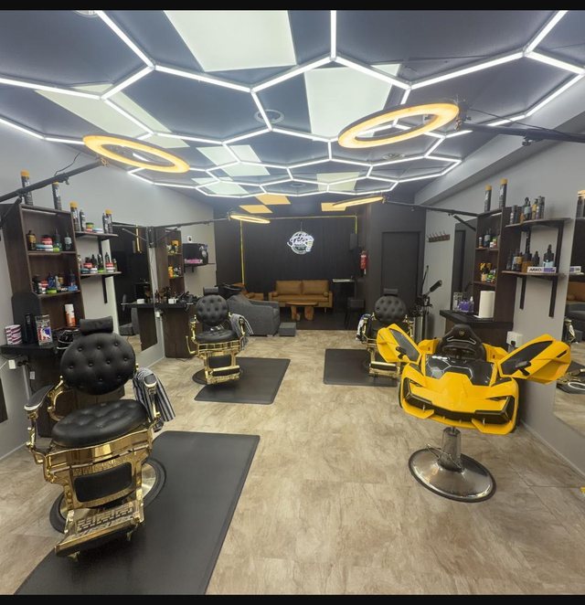 Inside Fade Shack Barbers, Orewa — honeycomb hex ceiling lights, ornate gold barber chairs, and the yellow racing-car kids' chair on the floor.